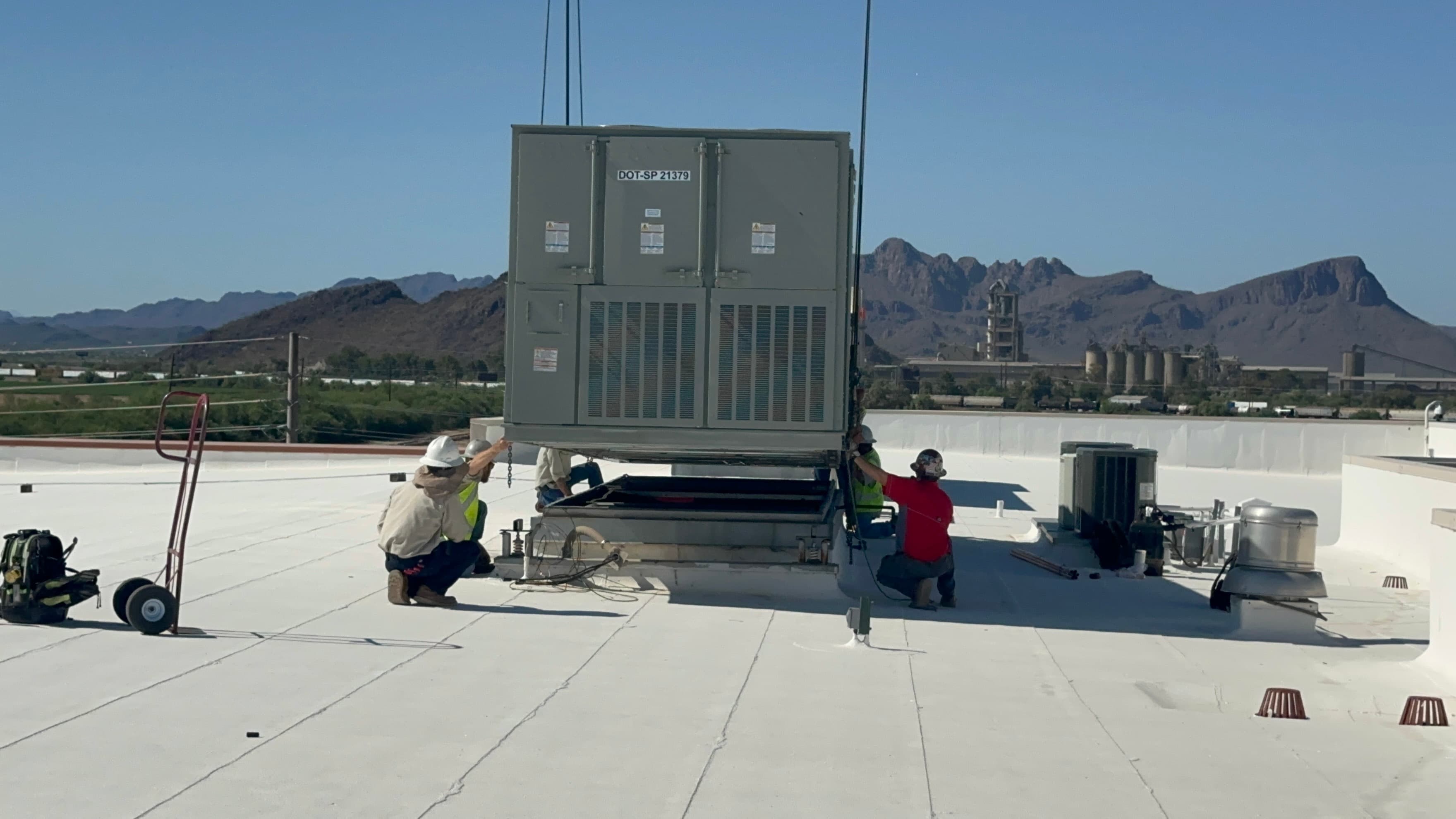 Two Air Excellence technicians setting a rooftop package unit with the Tucson mountains behind them
