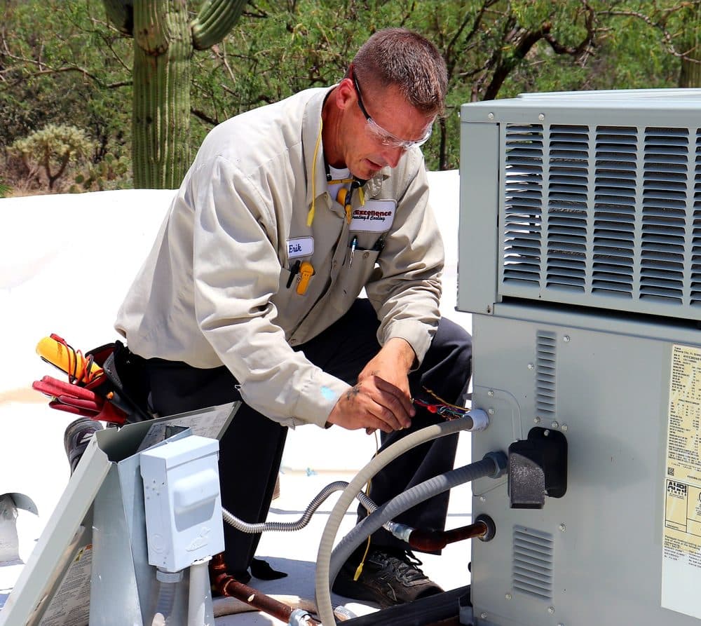 Air Excellence technician Erik wiring an outdoor condensing unit beside a saguaro at a Tucson home